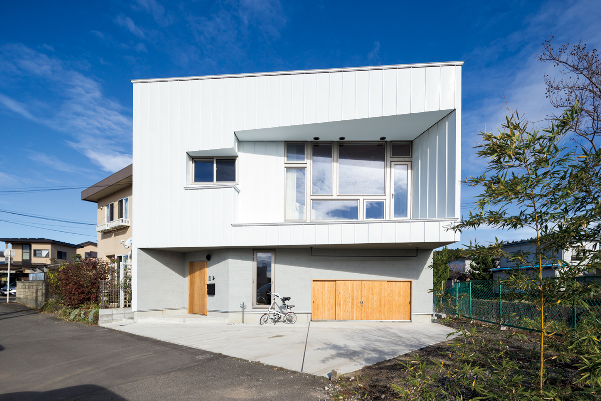 五角形の敷地に建つ不規則な四角形の家。外壁は玄関まわりはジョリパット、その他はガルバリウム鋼板仕上げ。中2階のリビングの床下は外物置とし、敷地に余裕のない狭小地のハンデをクリア