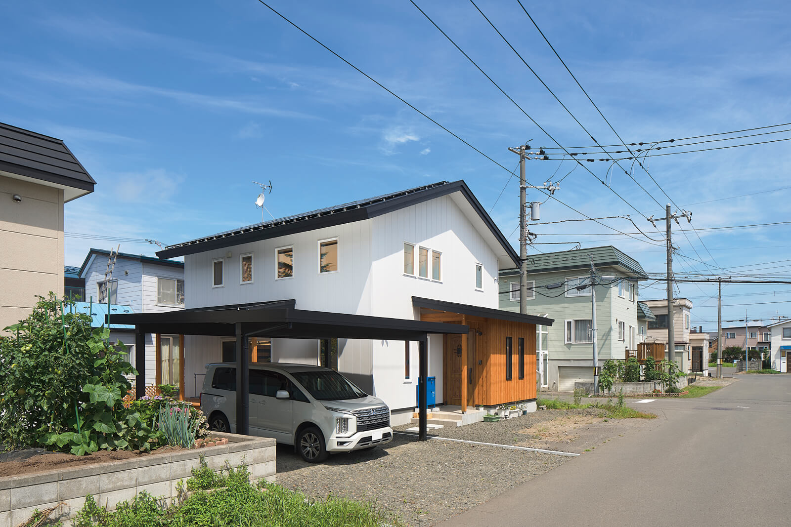 三角屋根と整然と並ぶ窓、アプローチの道南スギが特徴の外観。屋根には7.8kWの太陽光発電パネルも搭載