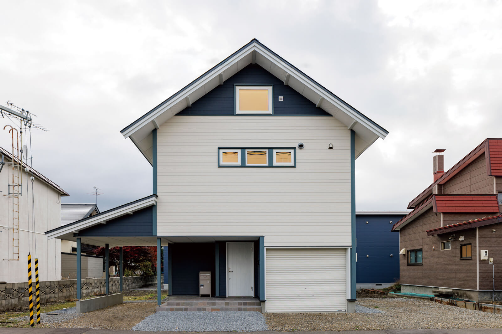 ブルーの濃淡と白でまとめ、三角屋根を採用した北欧住宅のような外観。ビルトインガレージのほか、建物と一体型の造作カーポートも設けた