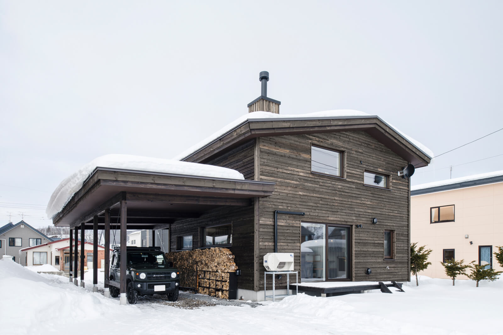 道南スギの外壁が雪景色の中になじむSさんご夫妻の住まい。玄関までカーポートの屋根があるため、雨や雪の日も濡れずに室内へと入ることができる