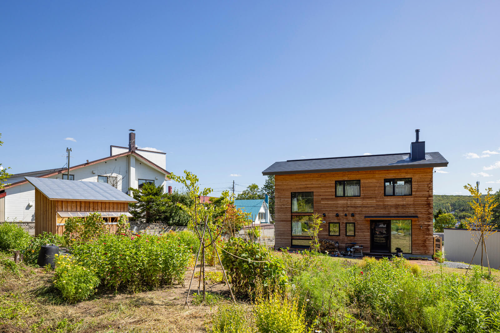 庭から建物を見る。傾斜地ならではの高さレベルのズレによって、住宅街にありながら心地よい視線の抜けが生まれた。奥さんが丹精する草花が咲く庭に、大工の手仕事を生かした作業小屋がしっくりとなじんでいる