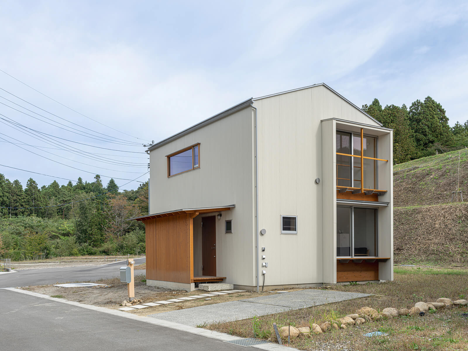 自然豊かな立地のKさん宅。オフホワイトのガルバリウム鋼板の外観に、玄関まわりの木がアクセントを添える。南側にはパッシブ設計の要となる大開口をレイアウト。冬はダイニング深くまで日光を届け、夏は庇で陽射しを遮る