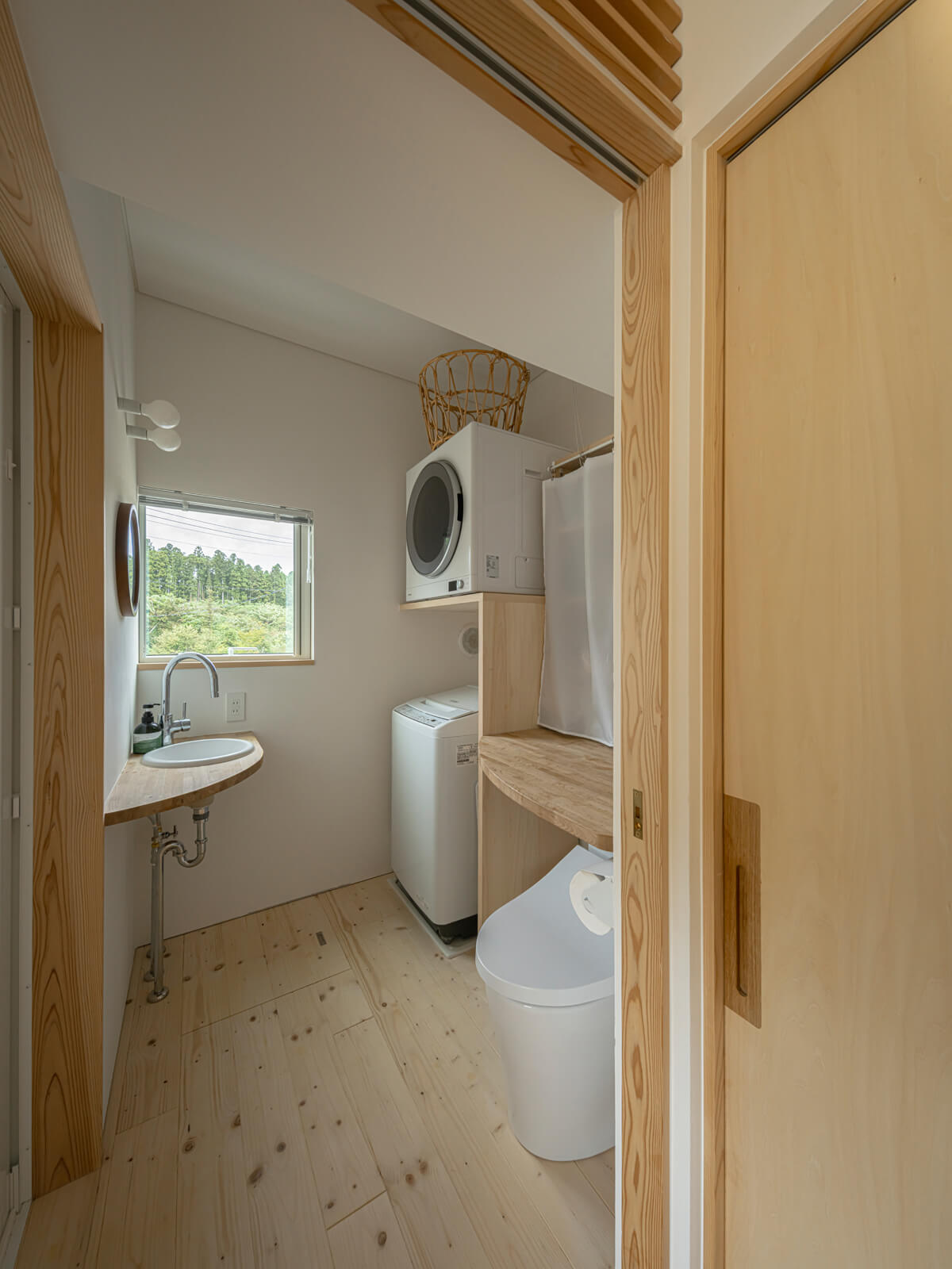 コンパクトながらも、窓のおかげで開放感のある洗濯・脱衣室兼トイレ。跳ね上げ式の作業台の下にトイレを配置してスペースを節約する工夫も