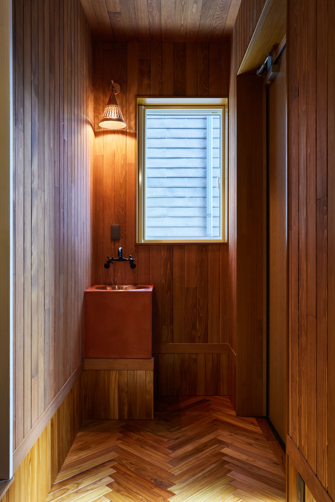 ヘリンボーンのフローリングにした玄関ホール。室内に入る前に手洗いができるようにコンパクトな洗面台を設置した。照明と洗面ボウルは銅製、天板はモールテックス仕上げ