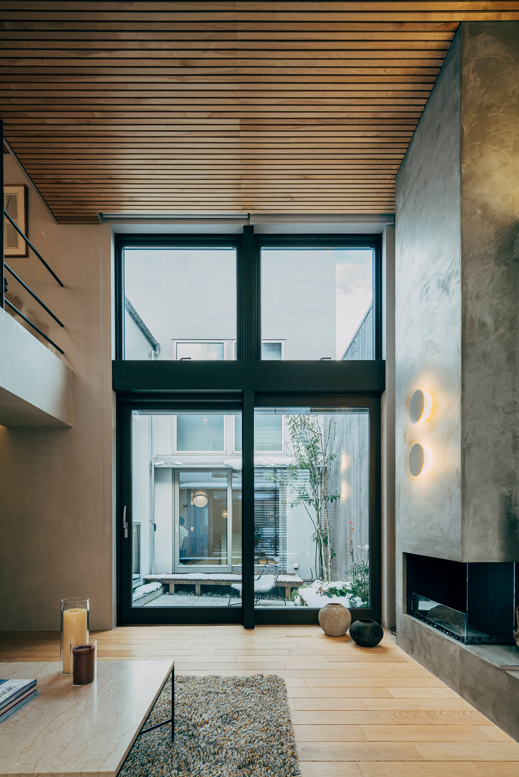 天井高約4.4ｍの吹き抜けが広がる12.5帖のリビング。暖炉のある壁は樹脂モルタルで仕上げて、石づくりのような印象になっている。幅3m、高さ約4mの大きな開口部は北側を向いているので、直射光が入らずやわらかい採光が確保できる