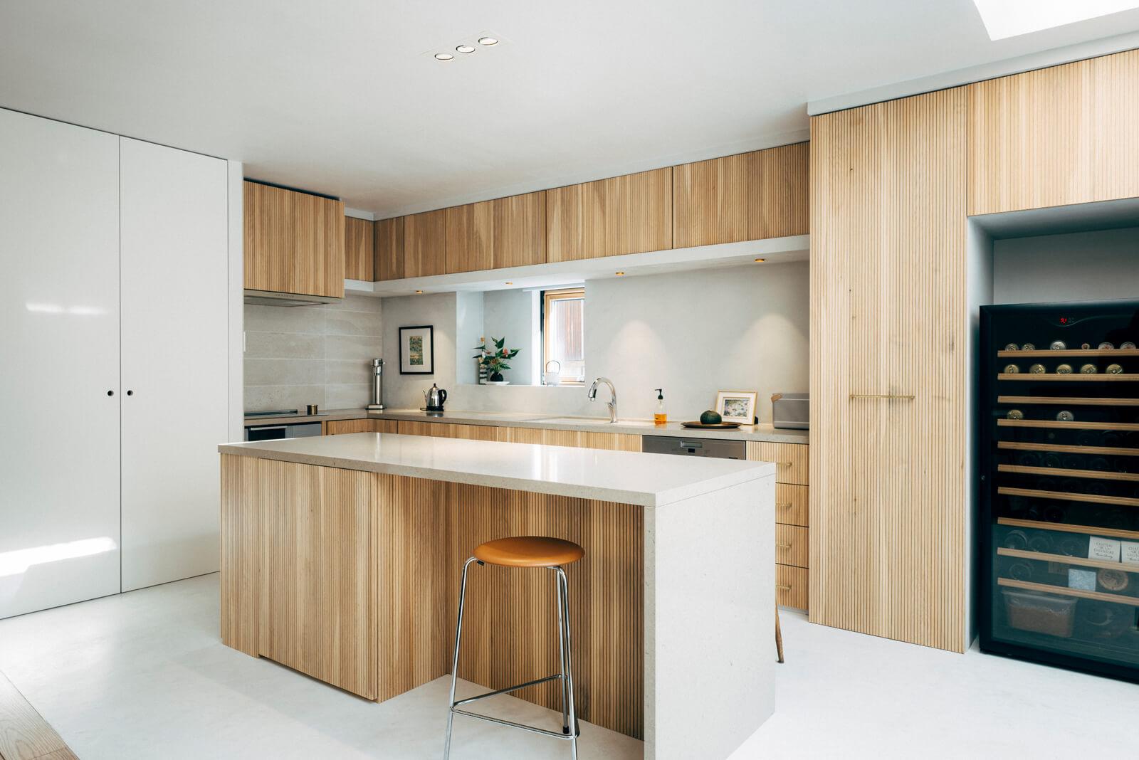 L字型キッチンには、広いアイランドの作業台を備えた。床はモールテックス仕上げ。リブ状に加工した北海道産ナラ材を開き戸に使った造作の隠せる収納は、収納力とデザイン性を兼ねそなえる。作業台にも収納が隠されている