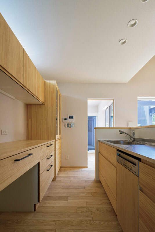 キッチンは無垢材の扉を多用して温かみのある仕上げに。吊り戸棚上部には朝陽を採り込めるように、スリット状のハイサイドライトをデザイン