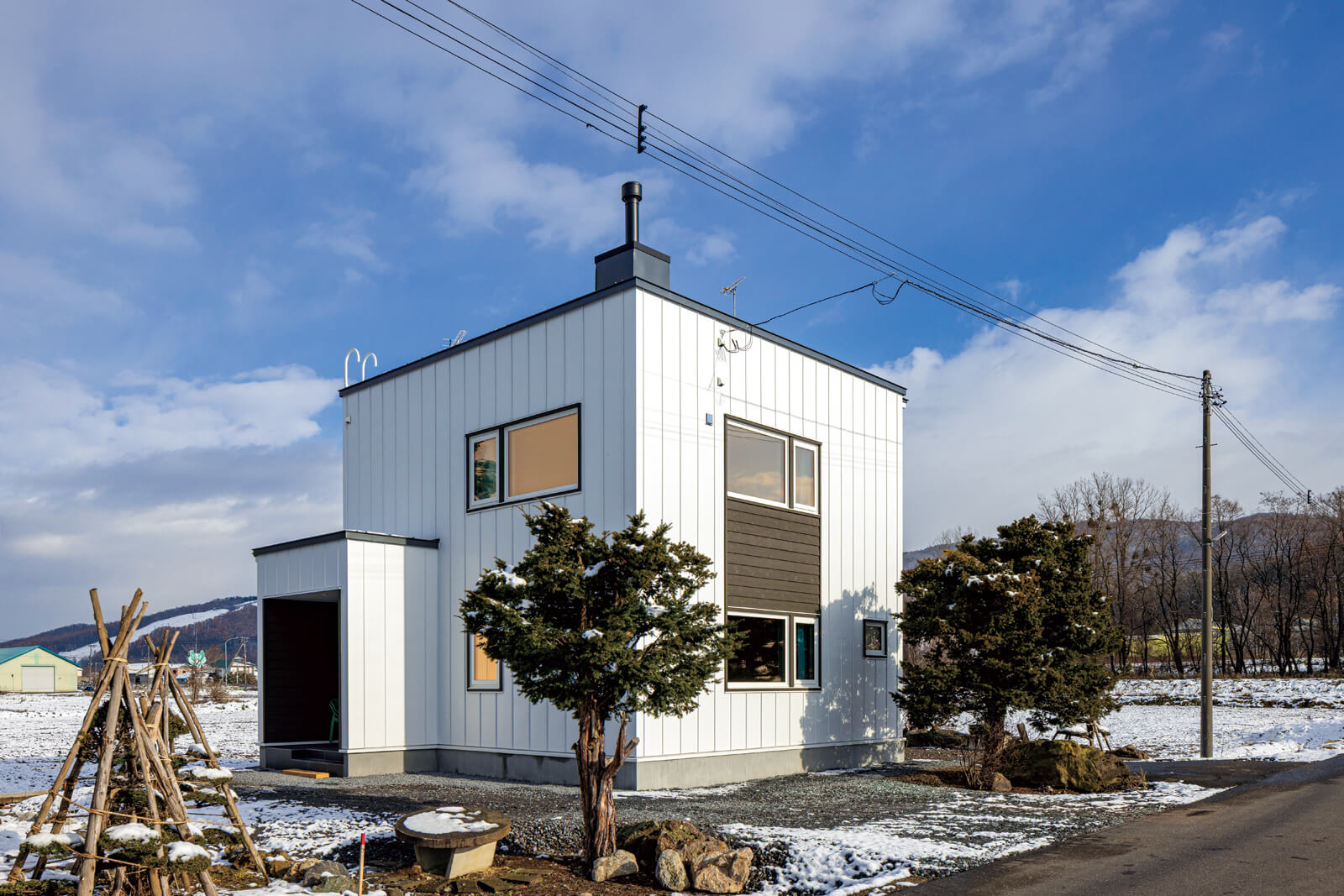ガルバリウム鋼板を採用したほぼキューブ型のフォルムがすっきりとした外観。道南スギ羽目板と薪ストーブの煙突がアクセント