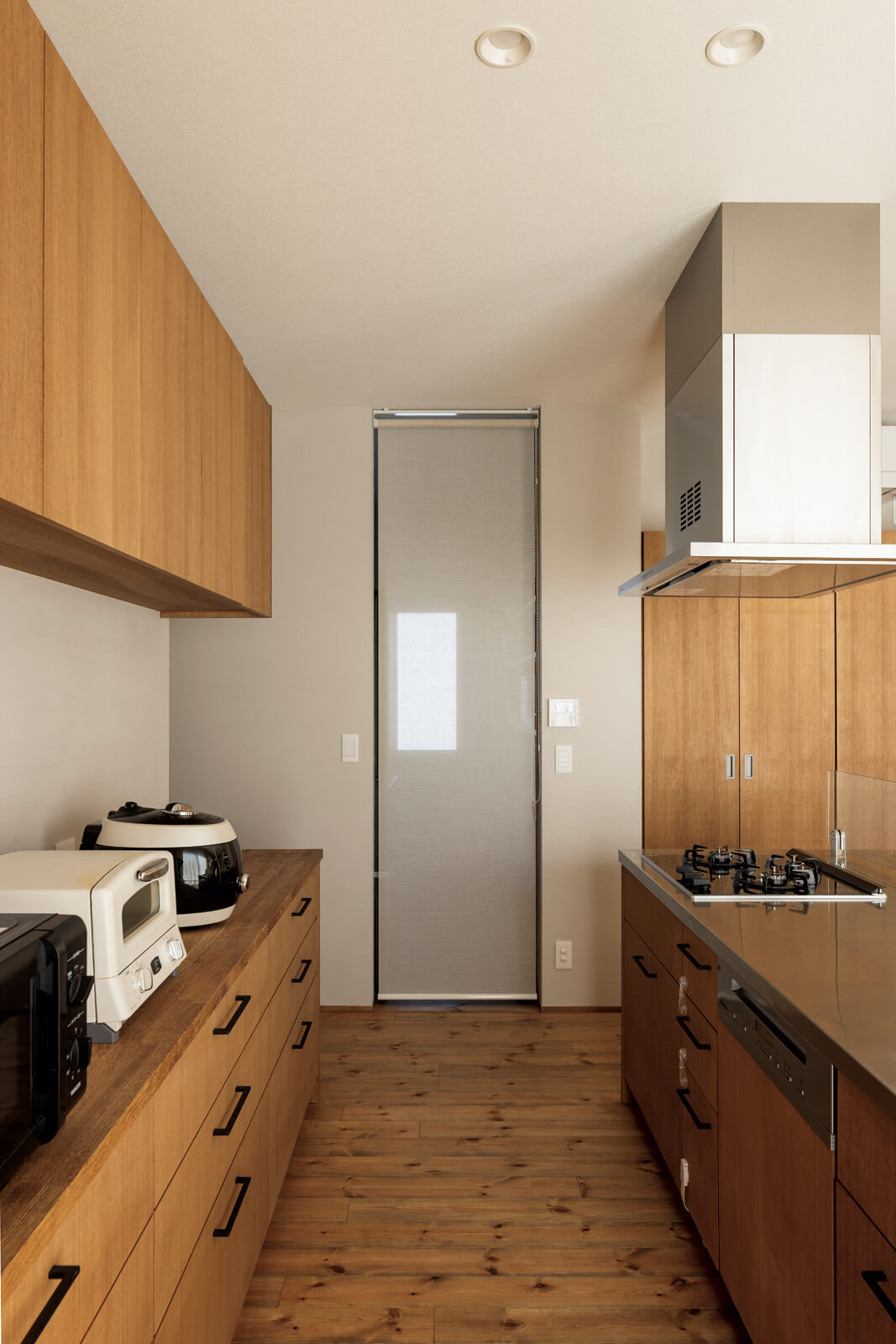 ナラの突板を用いて造作したアイランド型キッチンには、ミーレの大型食洗機も採用。背面には容量たっぷりの収納も造作した。ロールカーテン奥はパントリー