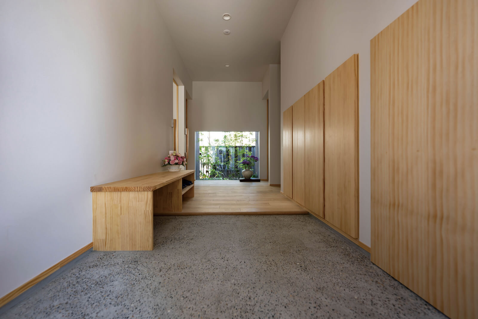 玄関は豆砂利洗い出し床仕上げ。正面の地窓を通して見える、きめ細かにデザインされた坪庭が、シンプルな空間を鮮やかに彩る